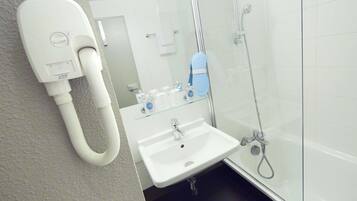 Une salle de bain avec un lavabo blanc, une douche en verre et un sèche-mains fixé au mur.