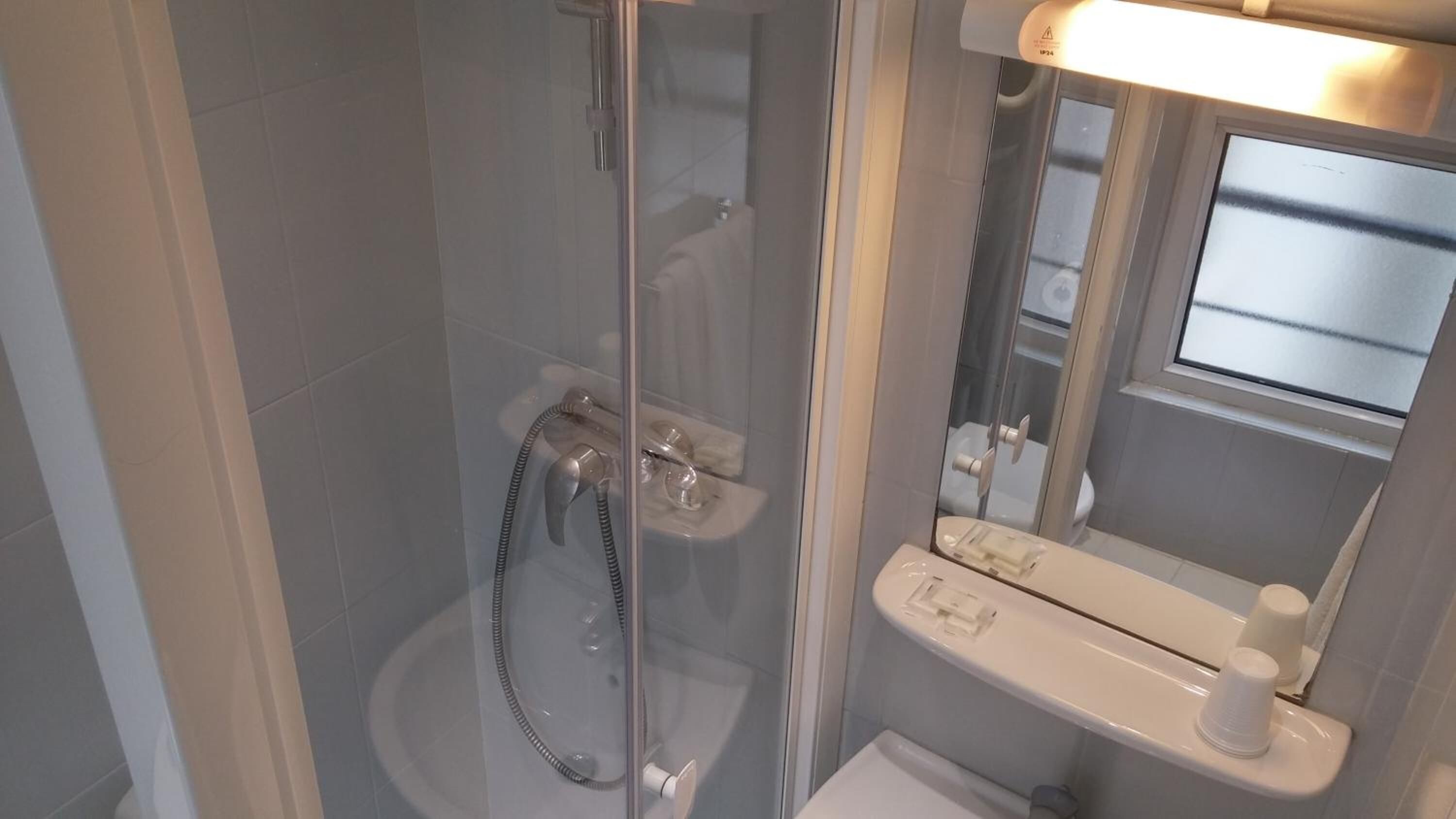 A modern shower enclosure with a glass door, a handheld showerhead, and a built-in mirror.