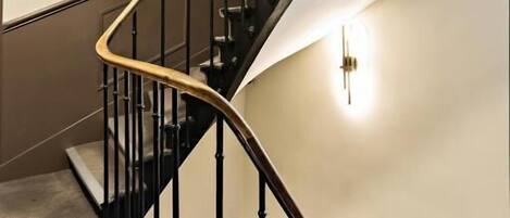 A curved staircase with black railings and a light fixture on the wall.