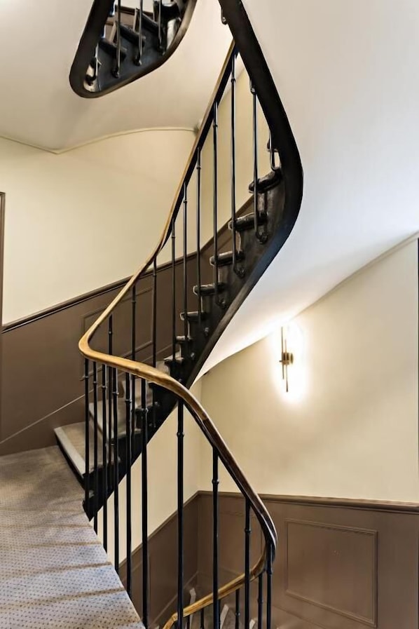 A curved staircase with black railings and a light fixture on the wall.