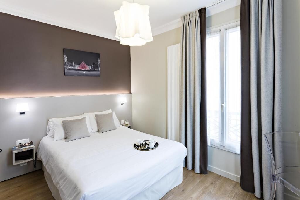 Una habitación de hotel moderna con una cama grande, mesitas de noche, una lámpara de pared y cortinas en la ventana.
