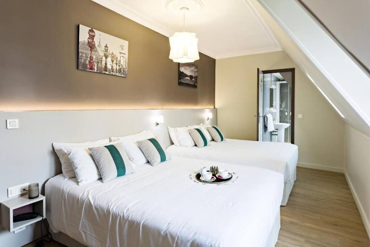 Habitación de hotel con dos camas, un cuadro en la pared, una mesita de noche y una bandeja con té y pasteles.