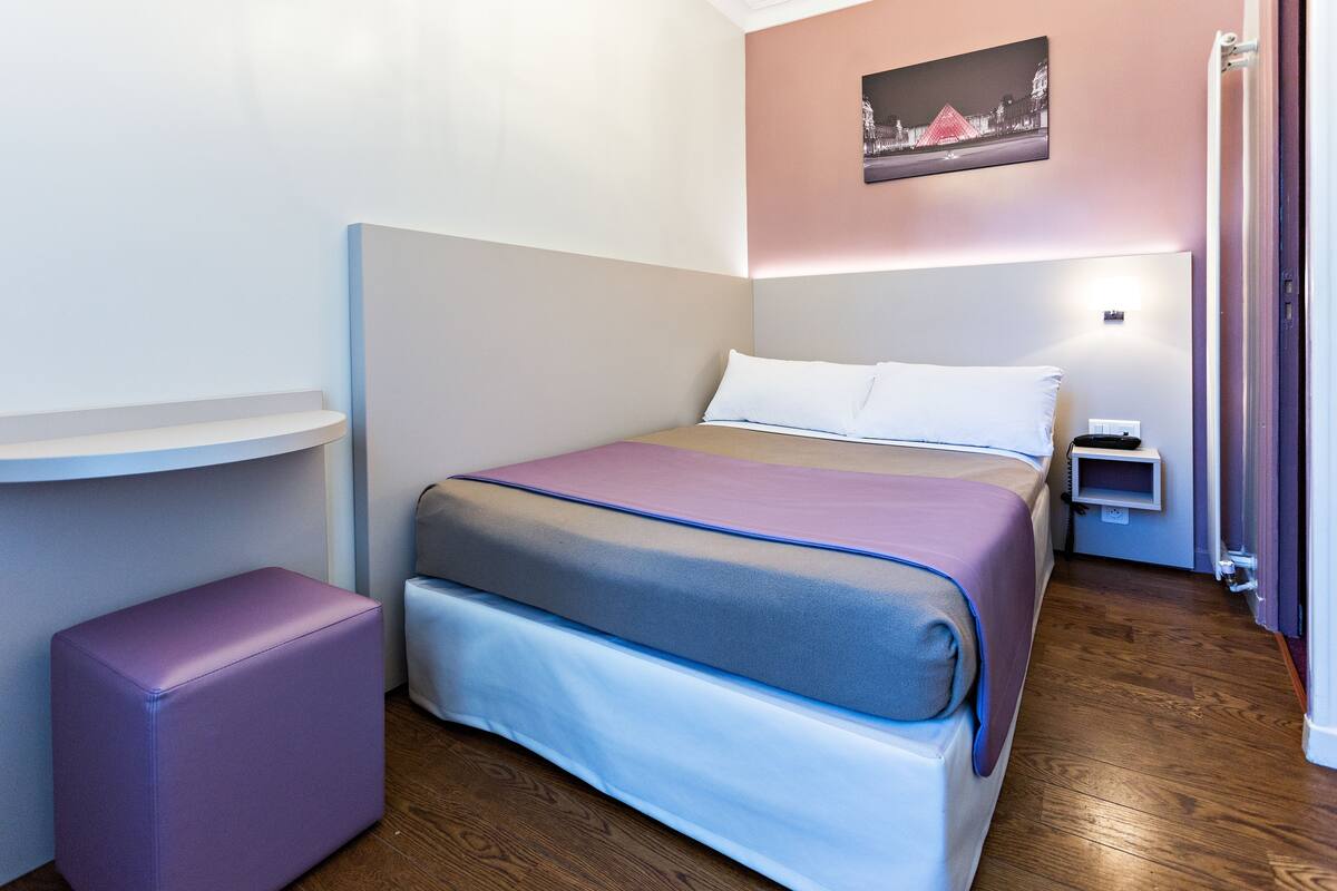 Habitación de hotel ordenada con cama, mesita de noche y estante fijado a la pared.