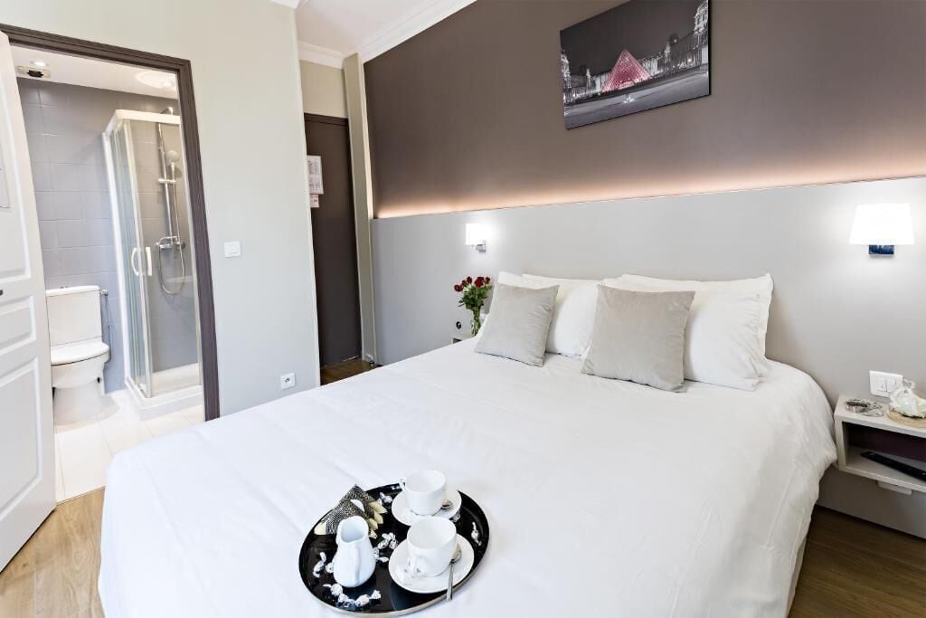 A hotel room with a bed, a bedside table, a nightstand, a glass shower enclosure, and a wall-mounted picture.
