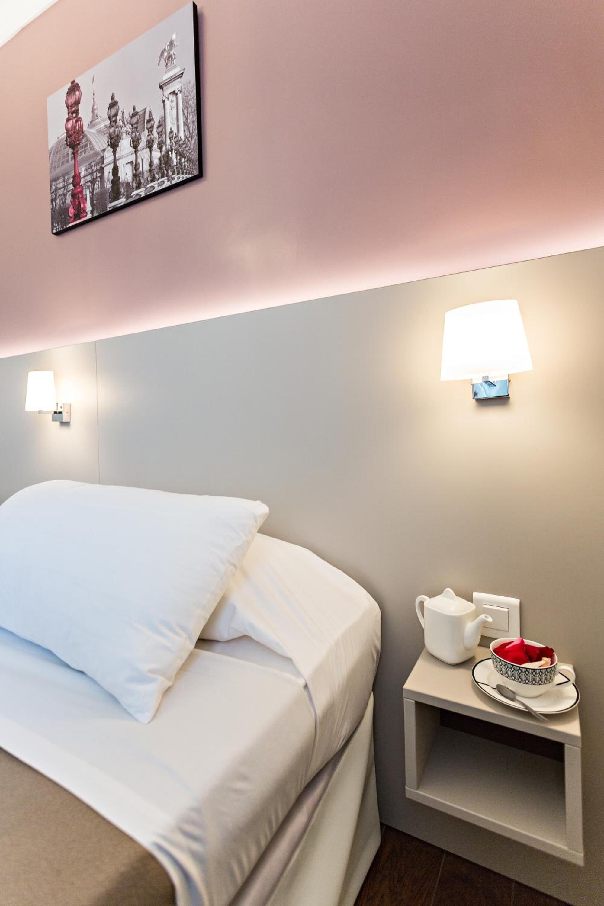 A neatly made bed with white linens, a small bedside table with a lamp, a cup, and a bowl.