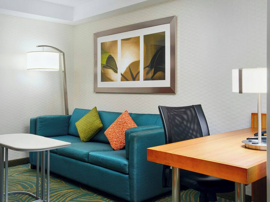 Ein Hotelzimmer mit einem türkisfarbenen Sofa, einem kleinen weißen Tisch, einem Holzbüro und einem gerahmten Kunstwerk an der Wand.