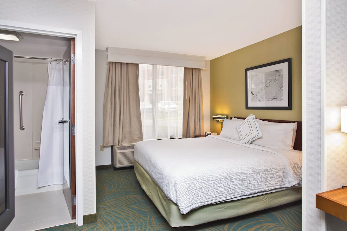A hotel room with a large bed, a shower area, and a window with curtains.