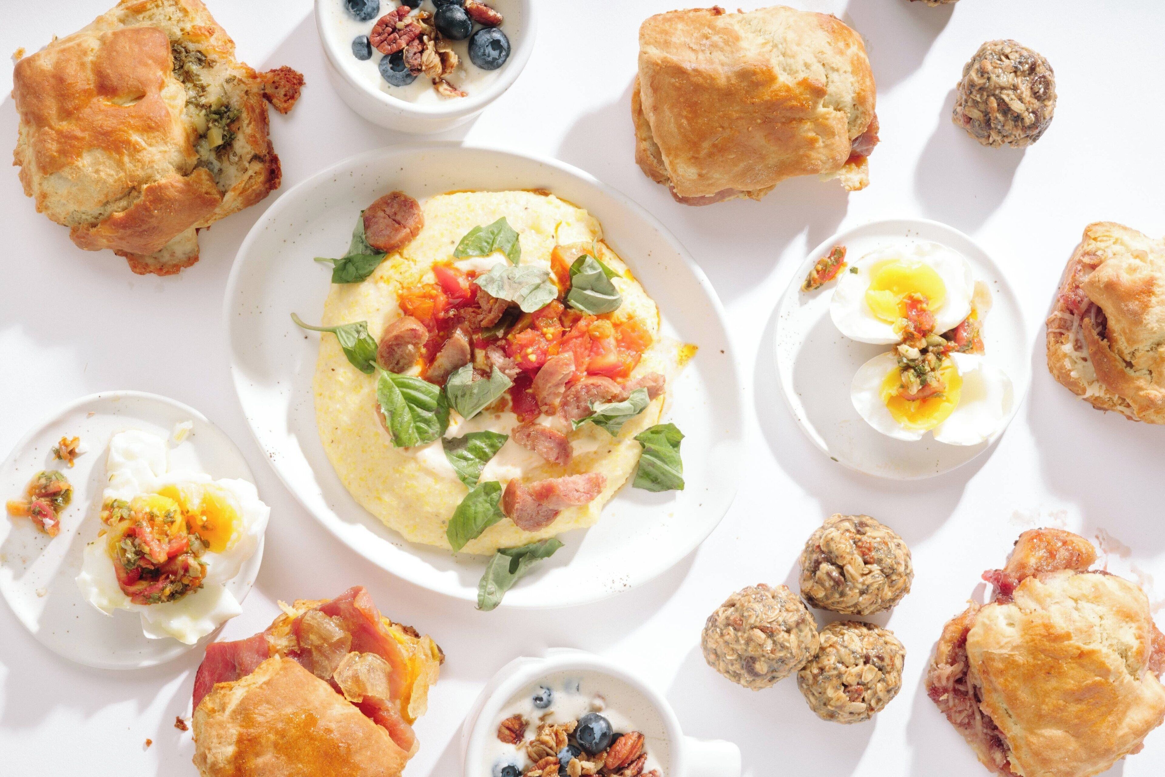 A breakfast spread with various pastries and a central dish of scrambled eggs with greens and bacon.