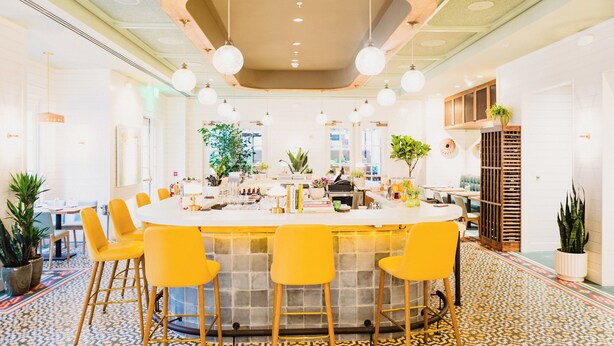 A modern bar area with a central island, yellow bar stools, and a patterned floor. - The Lindy Renaissance Charleston Hotel (Charleston)