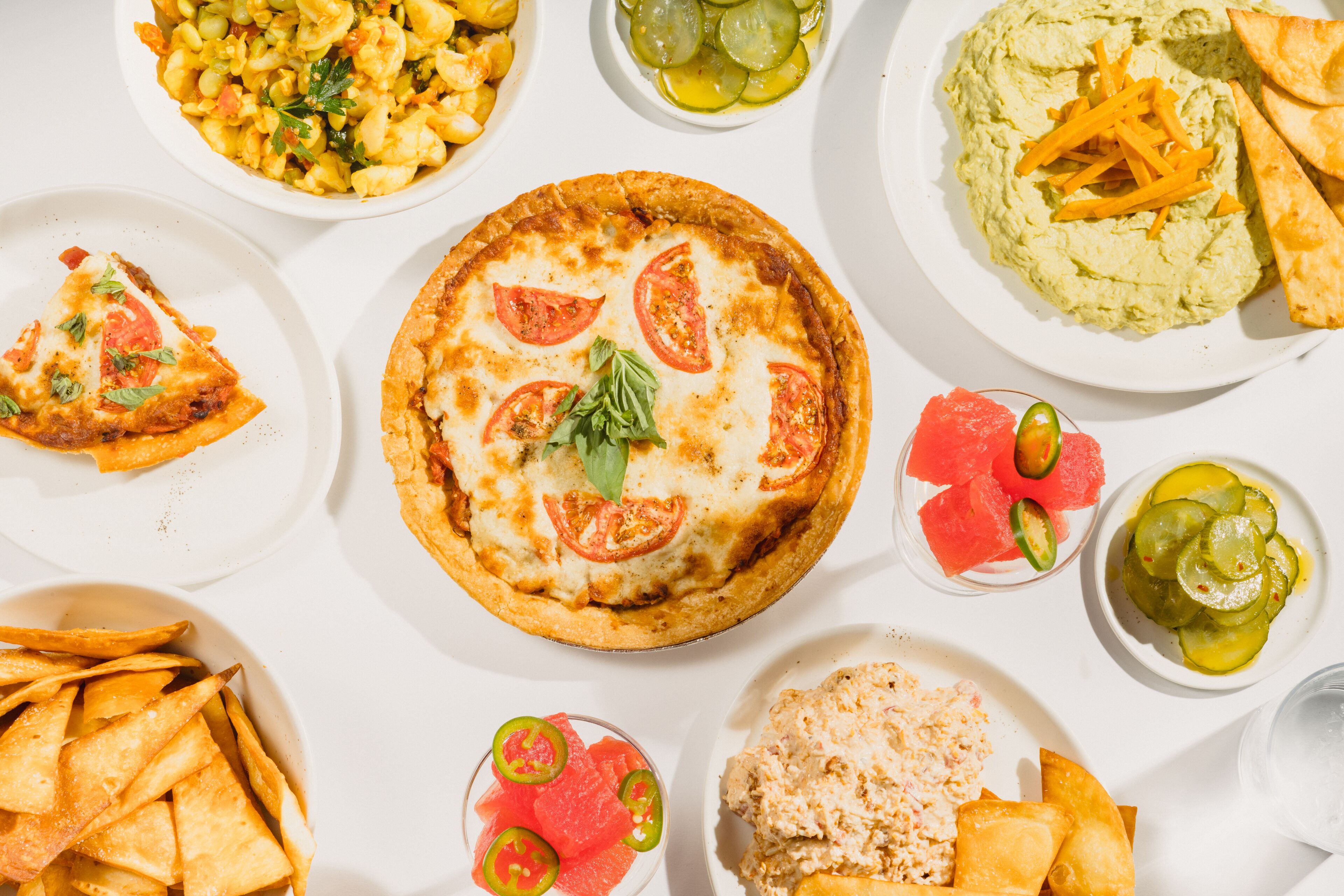 A variety of dishes including pizza, a quiche, and a bowl of guacamole.