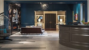 A modern interior with a dark blue accent wall, a seating area with a sofa and armchair, a fireplace, and a bar area with a decorative light fixture. - The Lindy Renaissance Charleston Hotel (Charleston)