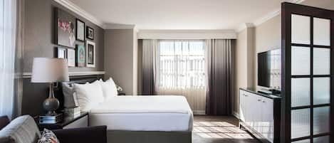Habitació d'hotel amb un llit, televisió, escriptori i finestra amb cortines.