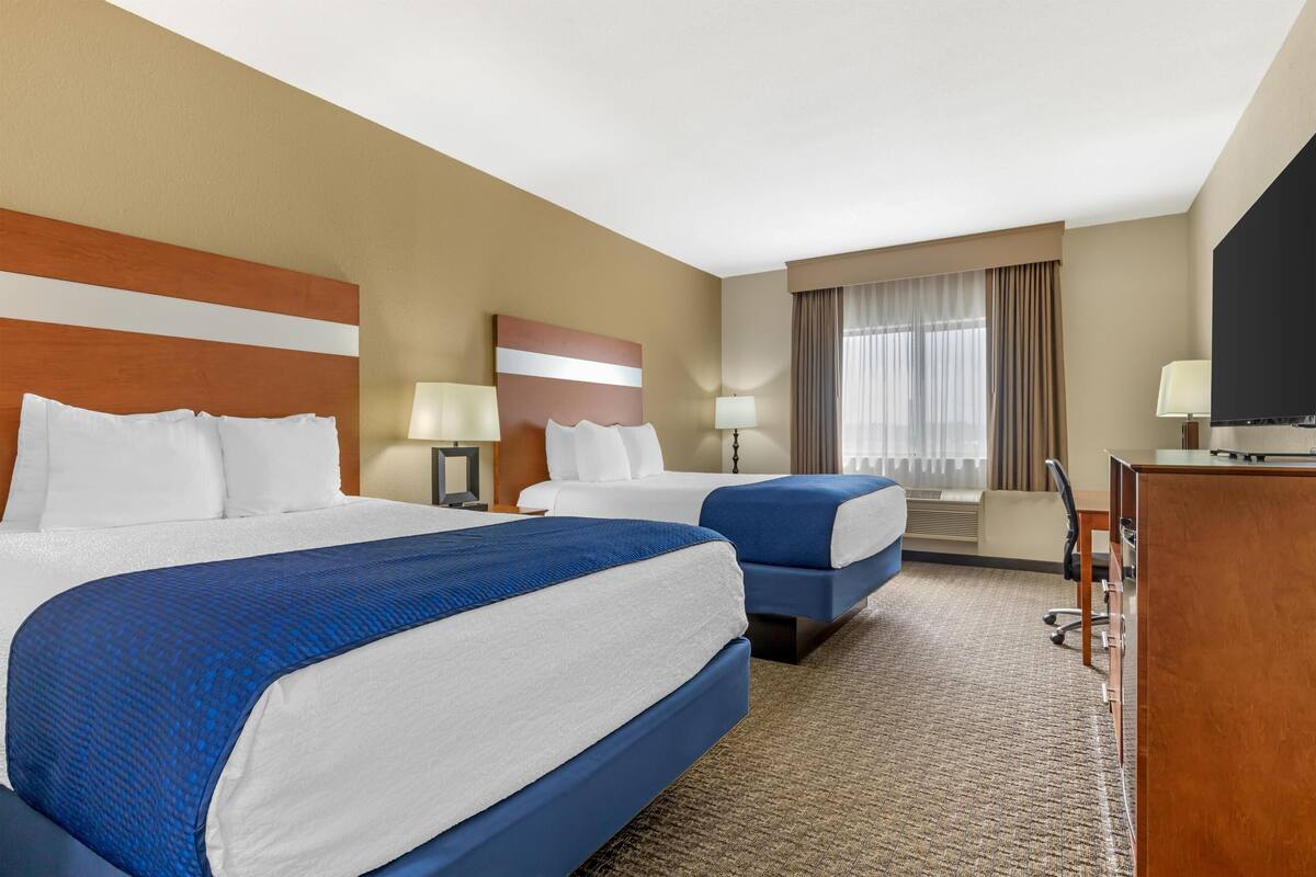A hotel room with two beds, a desk, a TV, and a window with curtains.