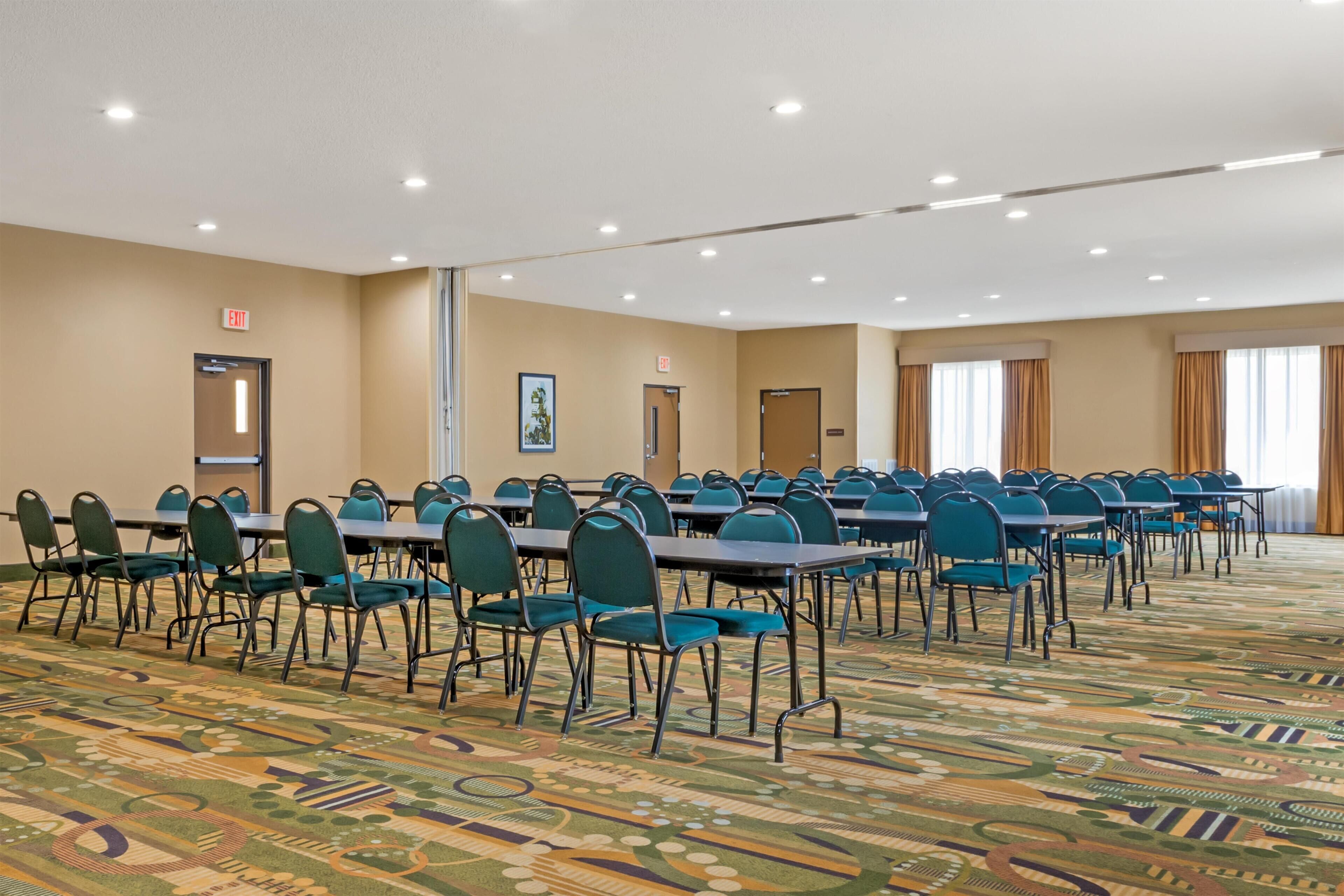 Une salle de conférence avec des rangées de tables et de chaises, un sol recouvert de moquette et des luminaires au plafond.