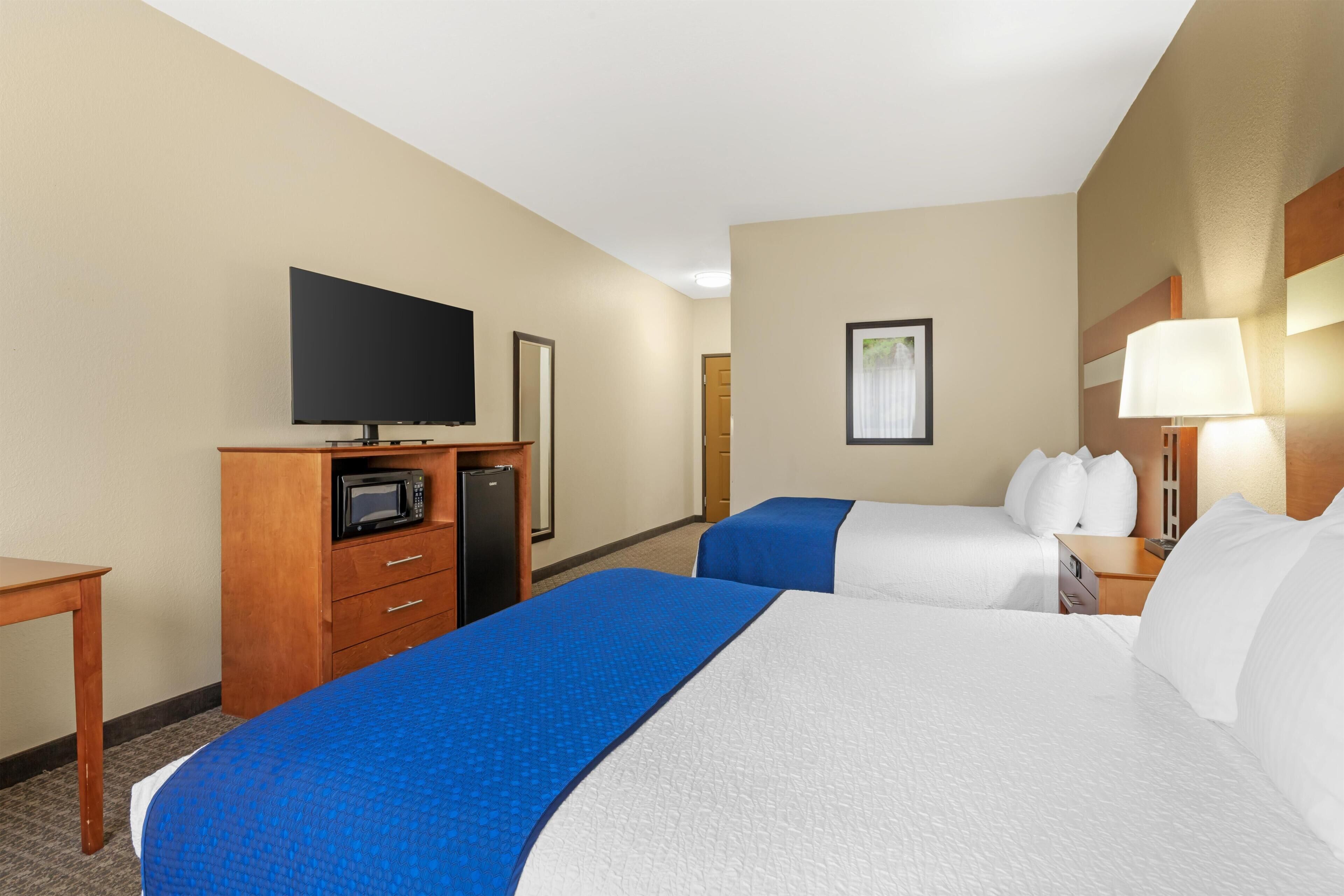 Een hotelkamer met twee bedden, een televisie, een magnetron en een bureau.