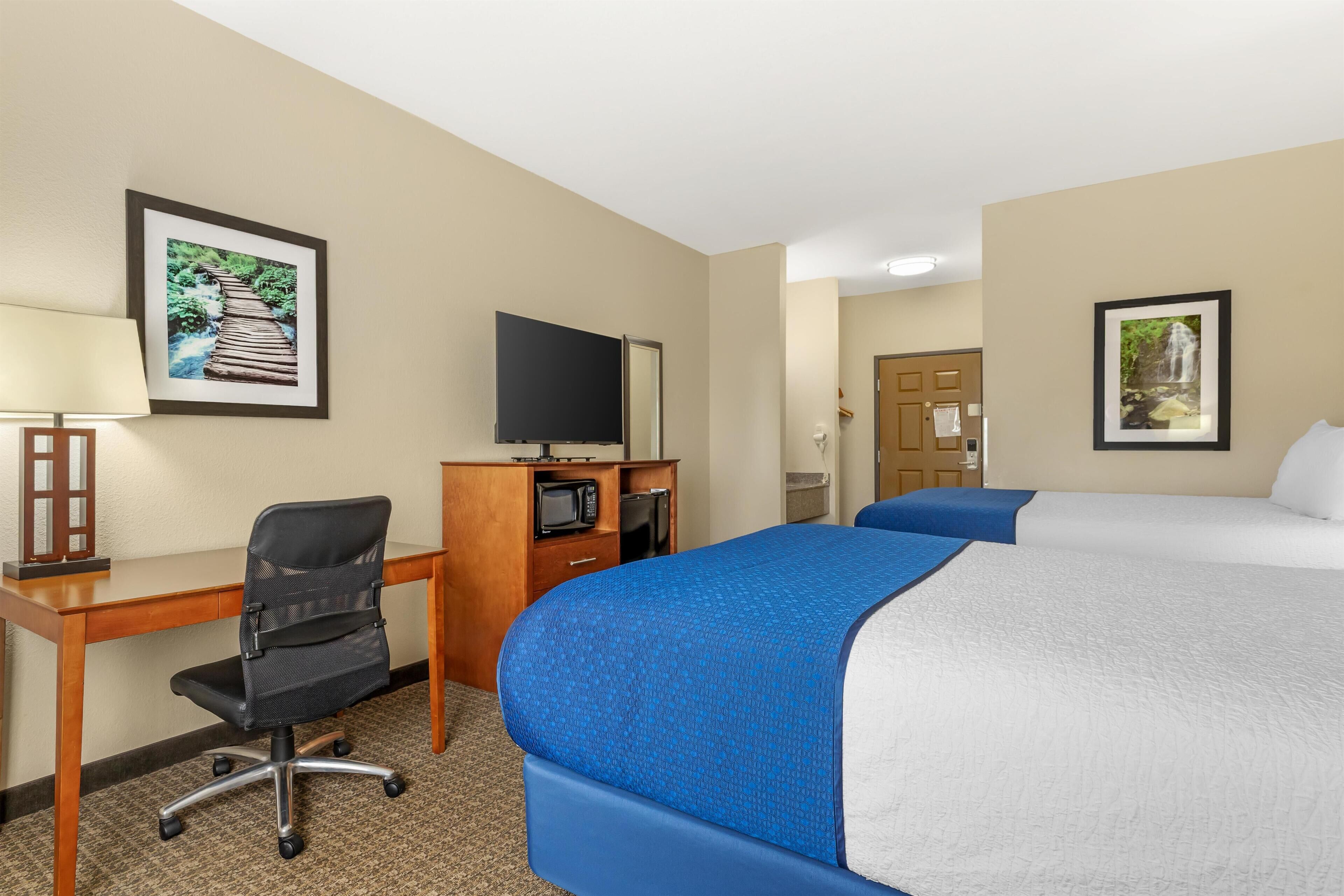 A hotel room with a bed, desk, chair, TV, and two framed pictures on the wall.