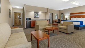 Ein Hotelzimmer mit einer Couch, zwei Sesseln, einem Couchtisch, einem Bett mit blauer Bettwäsche, einem Schreibtisch und einer Küchenzeile.