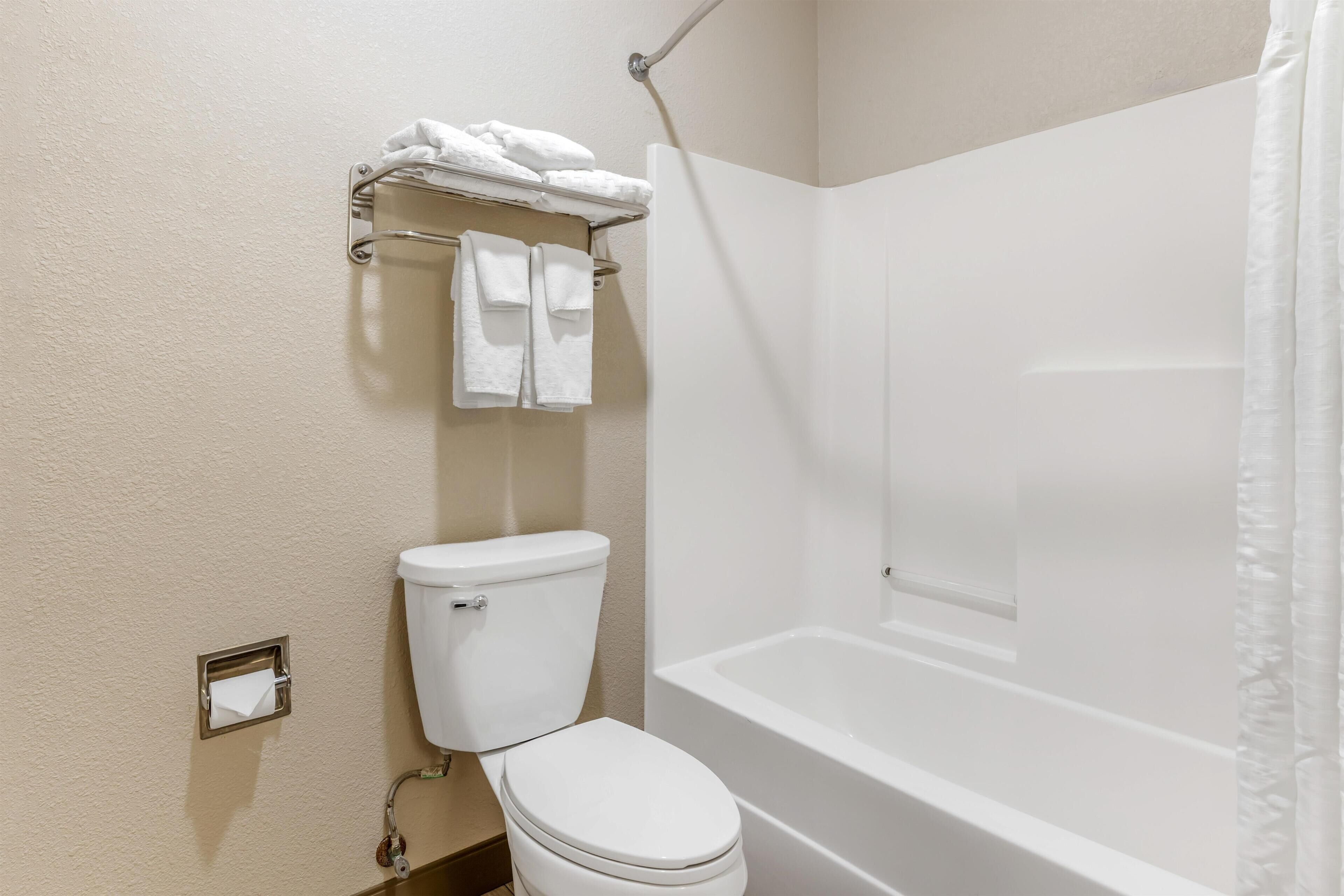 A bathroom with a toilet, a towel rack with towels, a toilet paper holder, and a bathtub.