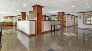 Eine Hotelhalle mit Empfangstresen, Holzelementen, einer Küchenzeile und einem glänzenden Boden.