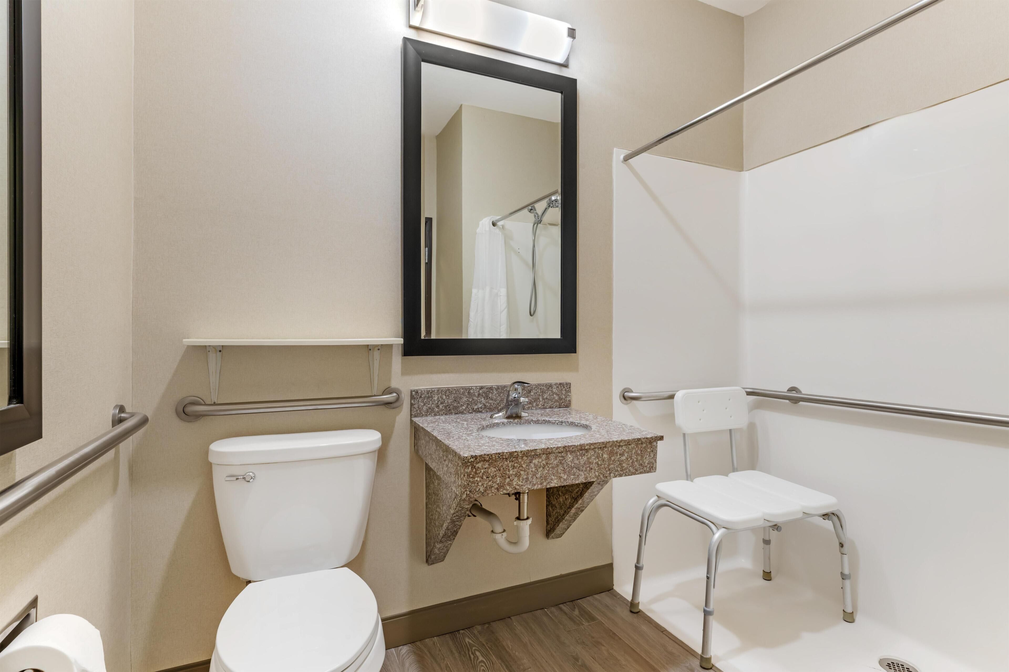 Een badkamer met toilet, wastafel, spiegel, douche en een rolstoeltoegankelijke stoel.