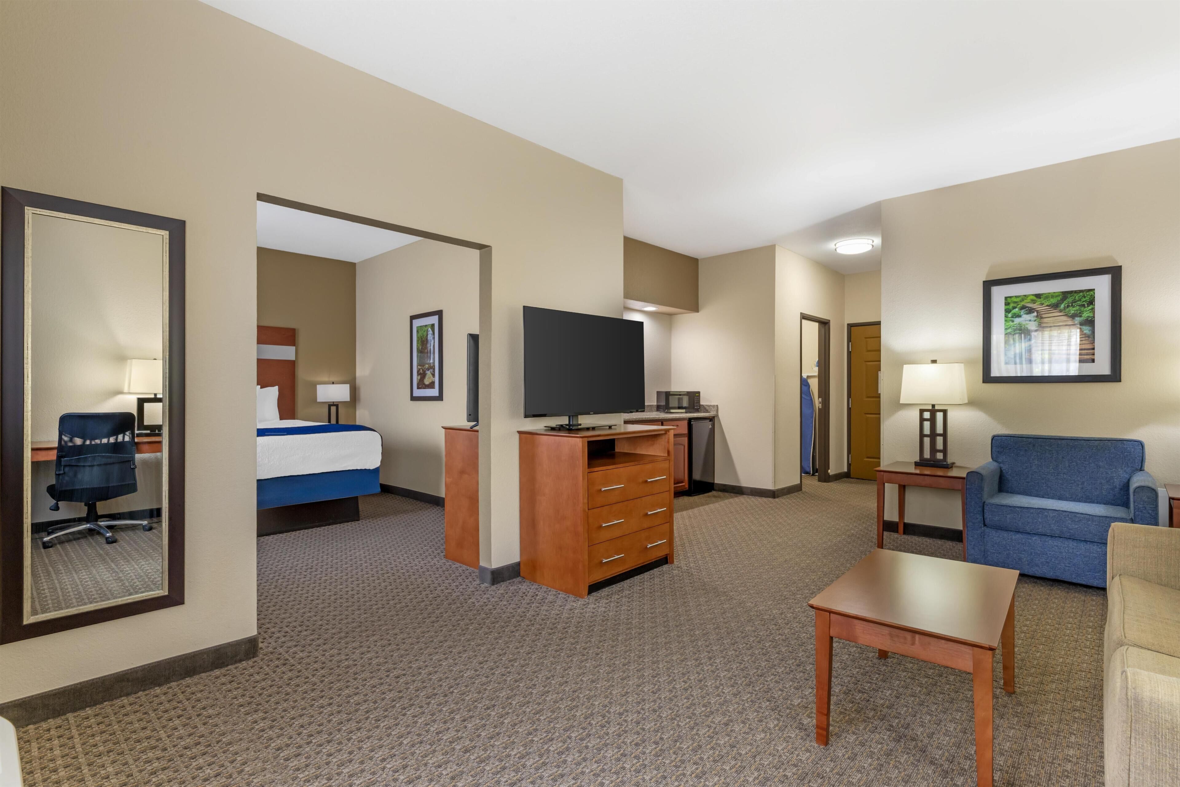 Une chambre d’hôtel avec un lit, un bureau avec un ordinateur, une télévision, un canapé bleu, une chaise et une petite table.