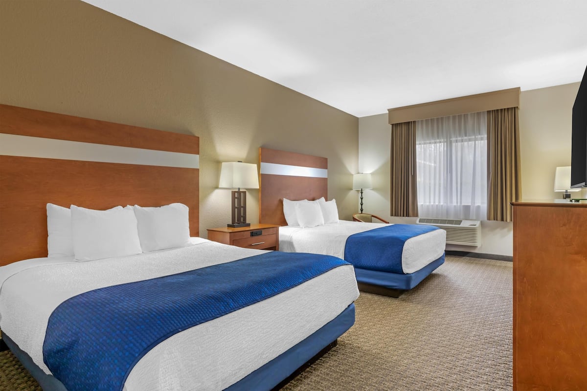 A hotel room with two beds, a desk, a lamp, a TV, and a window with curtains.