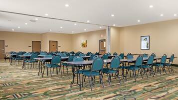 Un salón de conferencias con mesas y sillas dispuestas en filas, suelo alfombrado e iluminación en el techo.