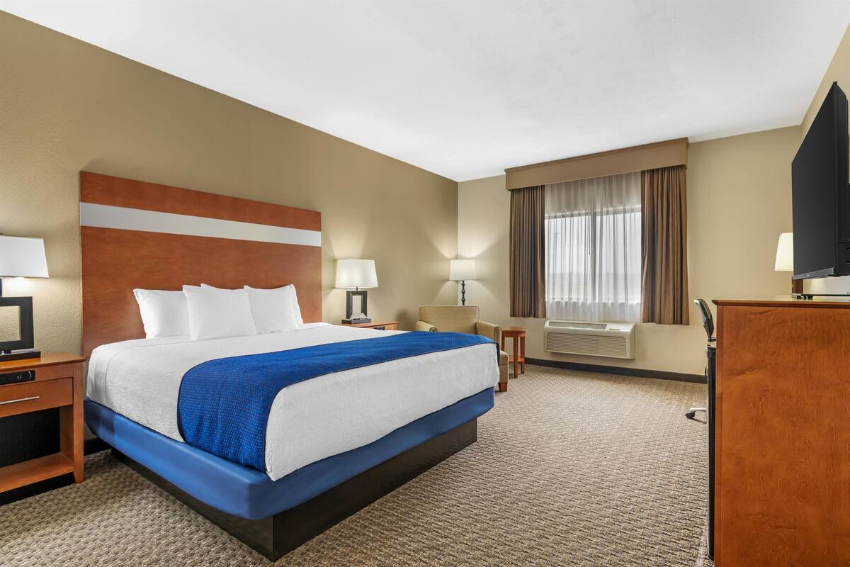 A hotel room with a large bed, a desk, a chair, a television, and a window with curtains.