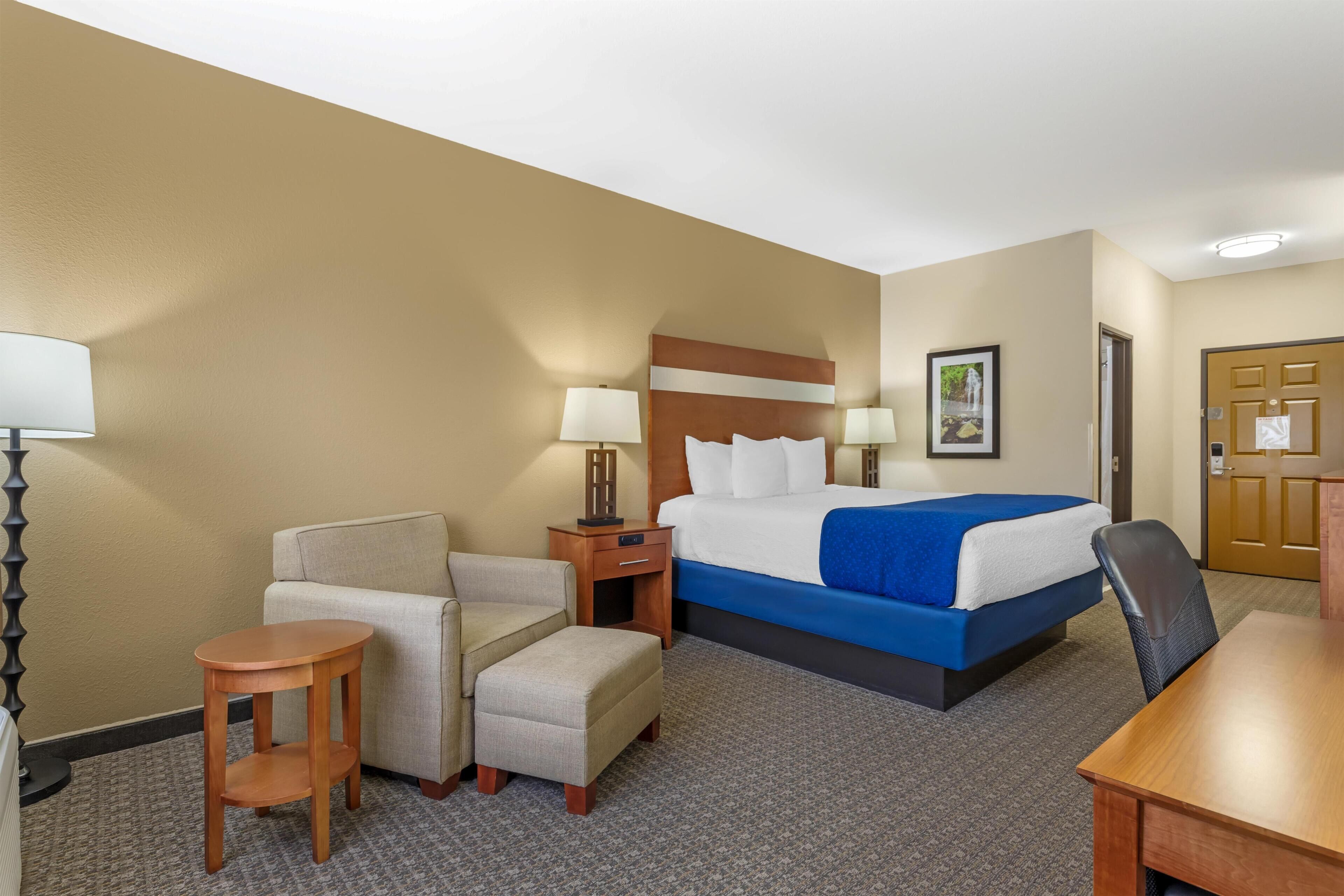 Een hotelkamer met een bed, een stoel, een klein tafeltje, een nachtkastje en een lamp.