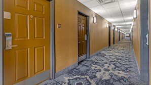 Ein Hotel-Flur mit Türen, einem gemusterten Teppich und einer Decke mit eingelassenen Leuchten.