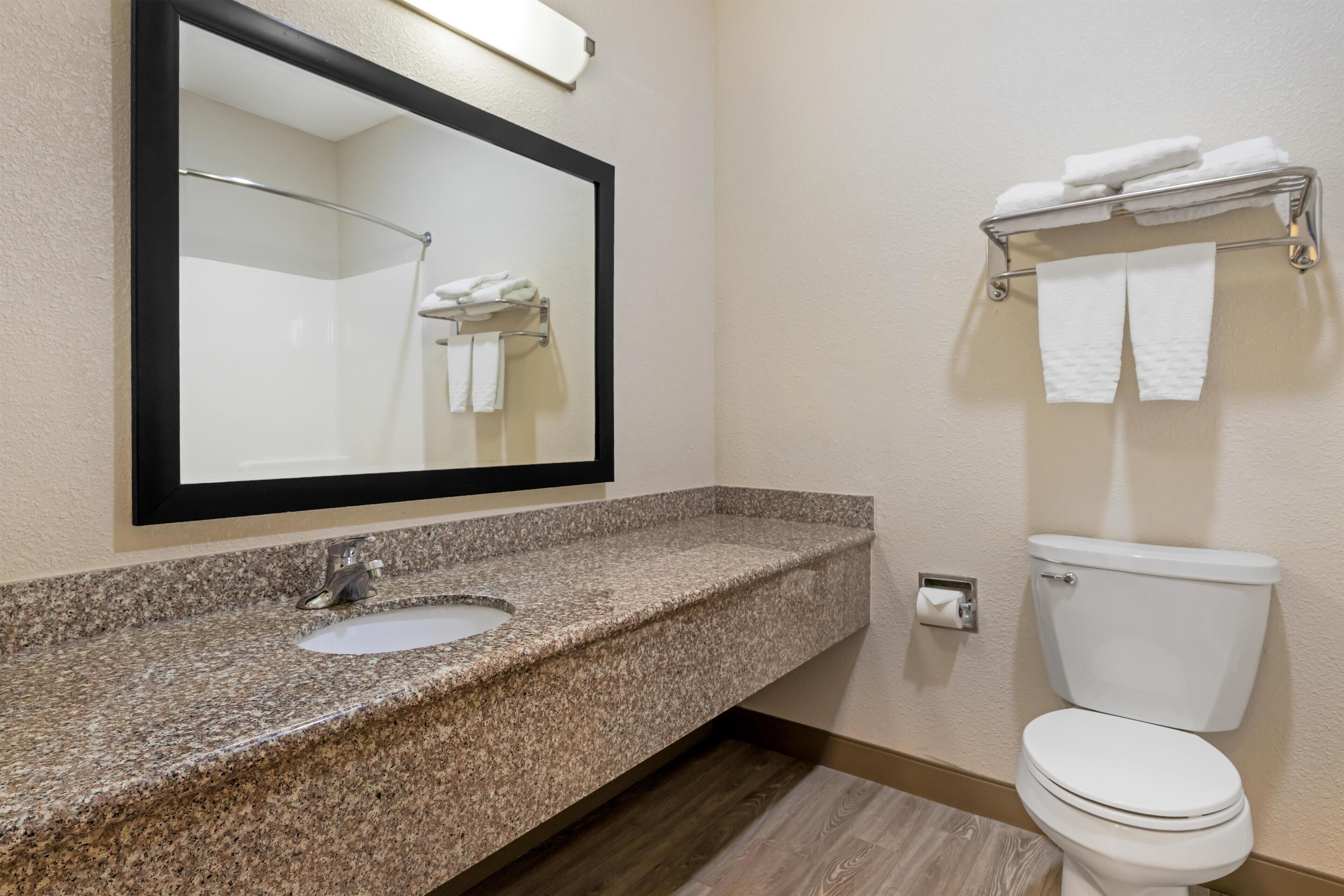 A bathroom with a granite countertop sink, a mirror, a toilet, and a towel rack.