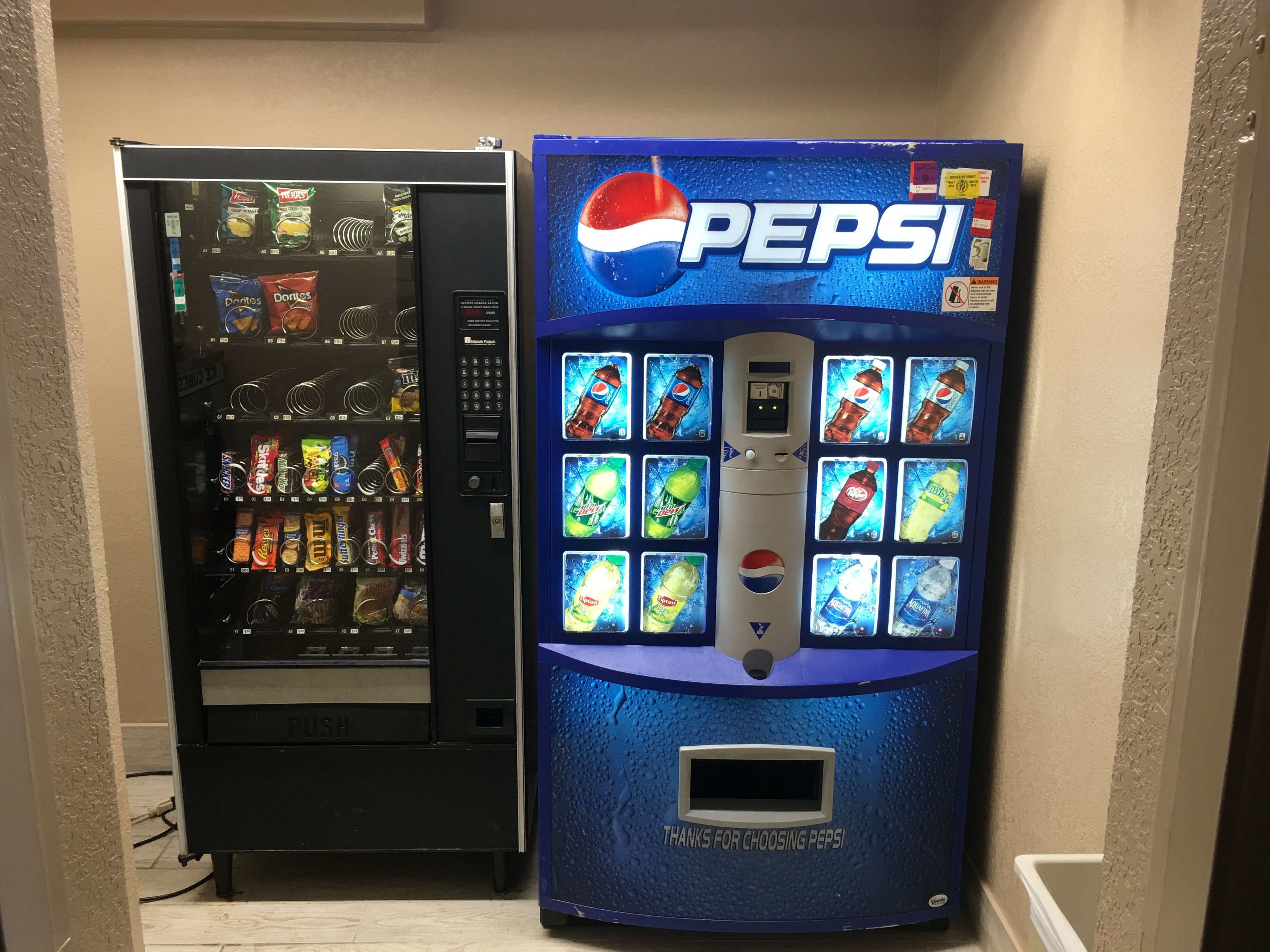 Two vending machines, one for Doritos and another for Pepsi, in a hallway.