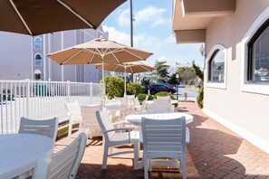 An outdoor patio with white plastic chairs and tables, a large umbrella, and a white fence. - Comfort Inn Ocean City Boardwalk (Ocean City)