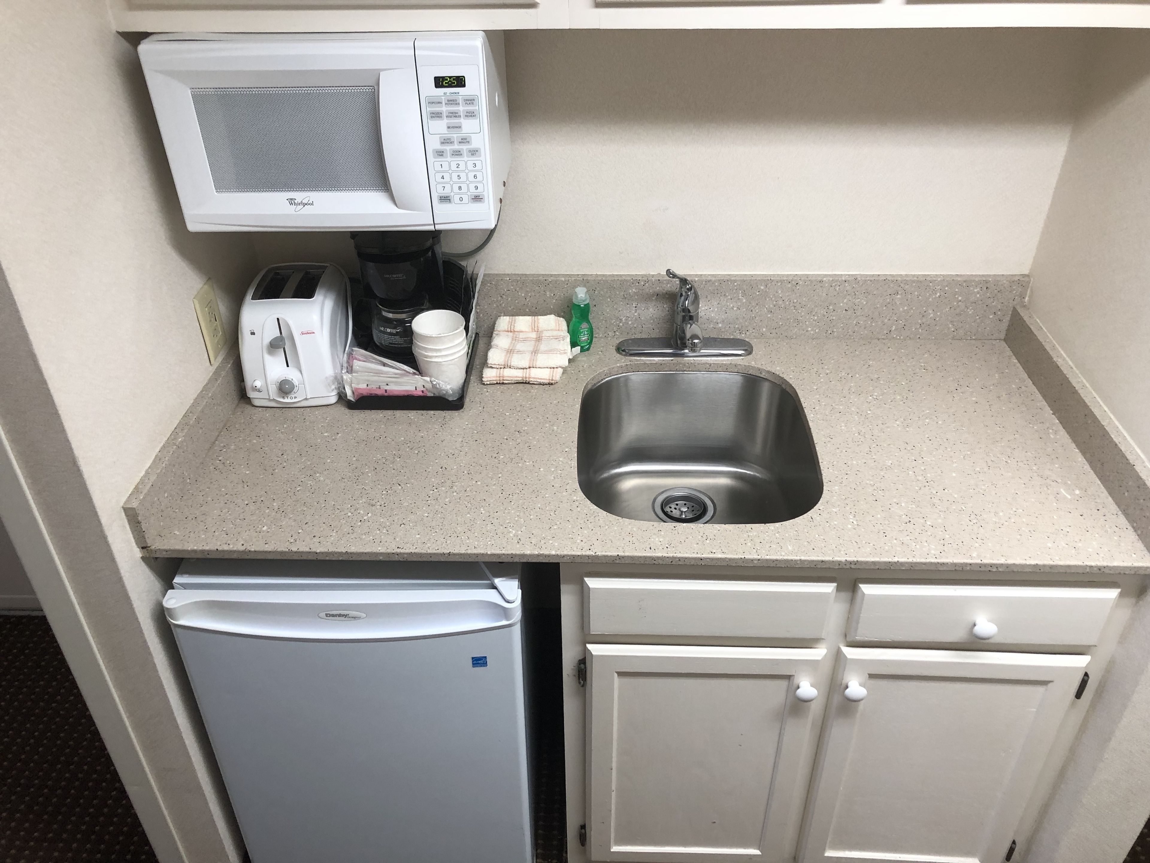 A compact kitchenette with a microwave, toaster, coffee maker, sink, and a refrigerator.