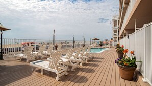 A deck with white lounge chairs and a pool, overlooking a beach. - Comfort Inn Ocean City Boardwalk (Ocean City)