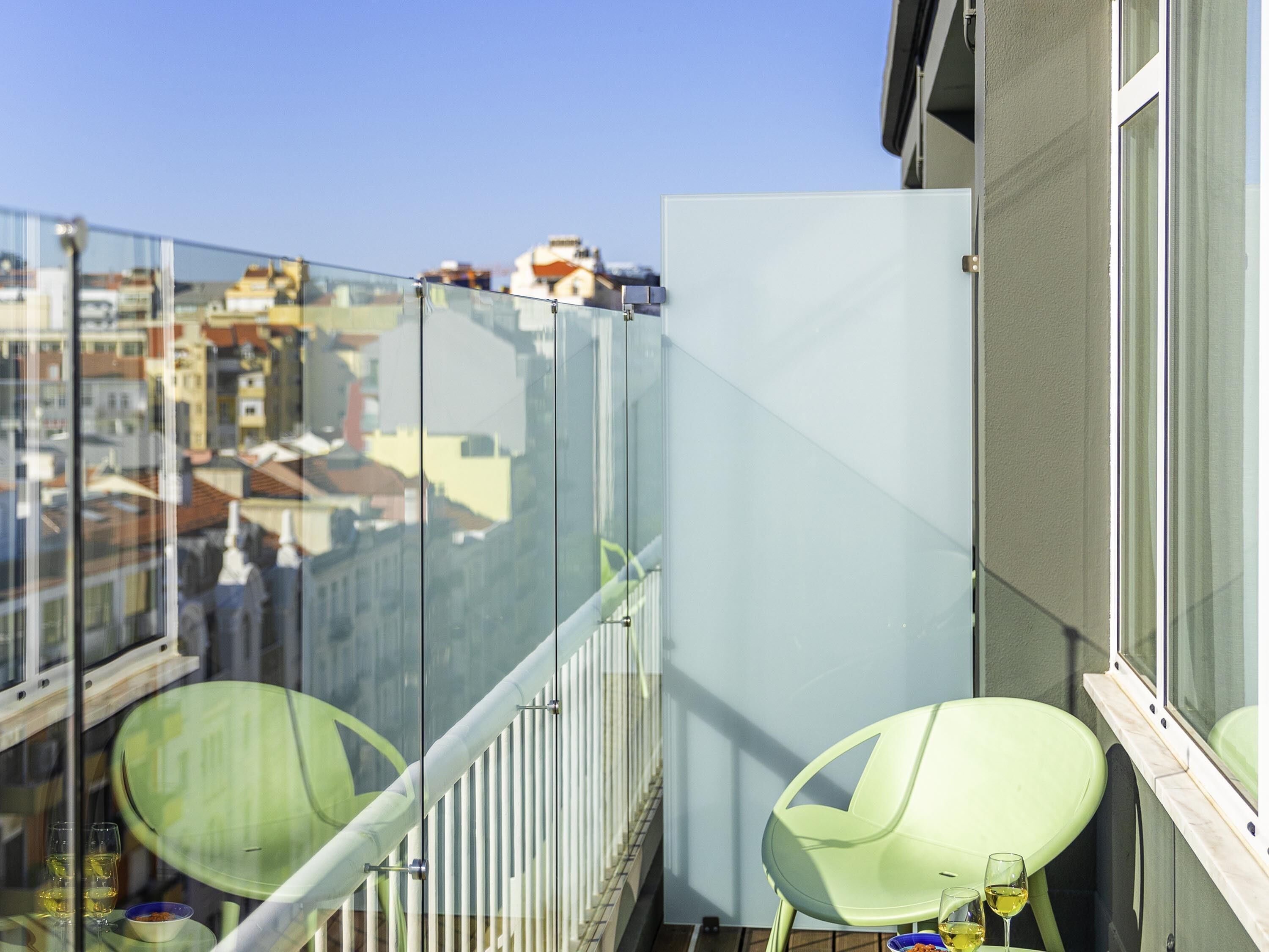A balcony with two green chairs, a glass railing, and a view of buildings.