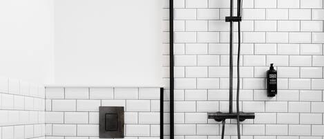 A modern bathroom with white subway tiles, a black and white patterned floor, a toilet, a shower with a handheld showerhead, and a towel rack.