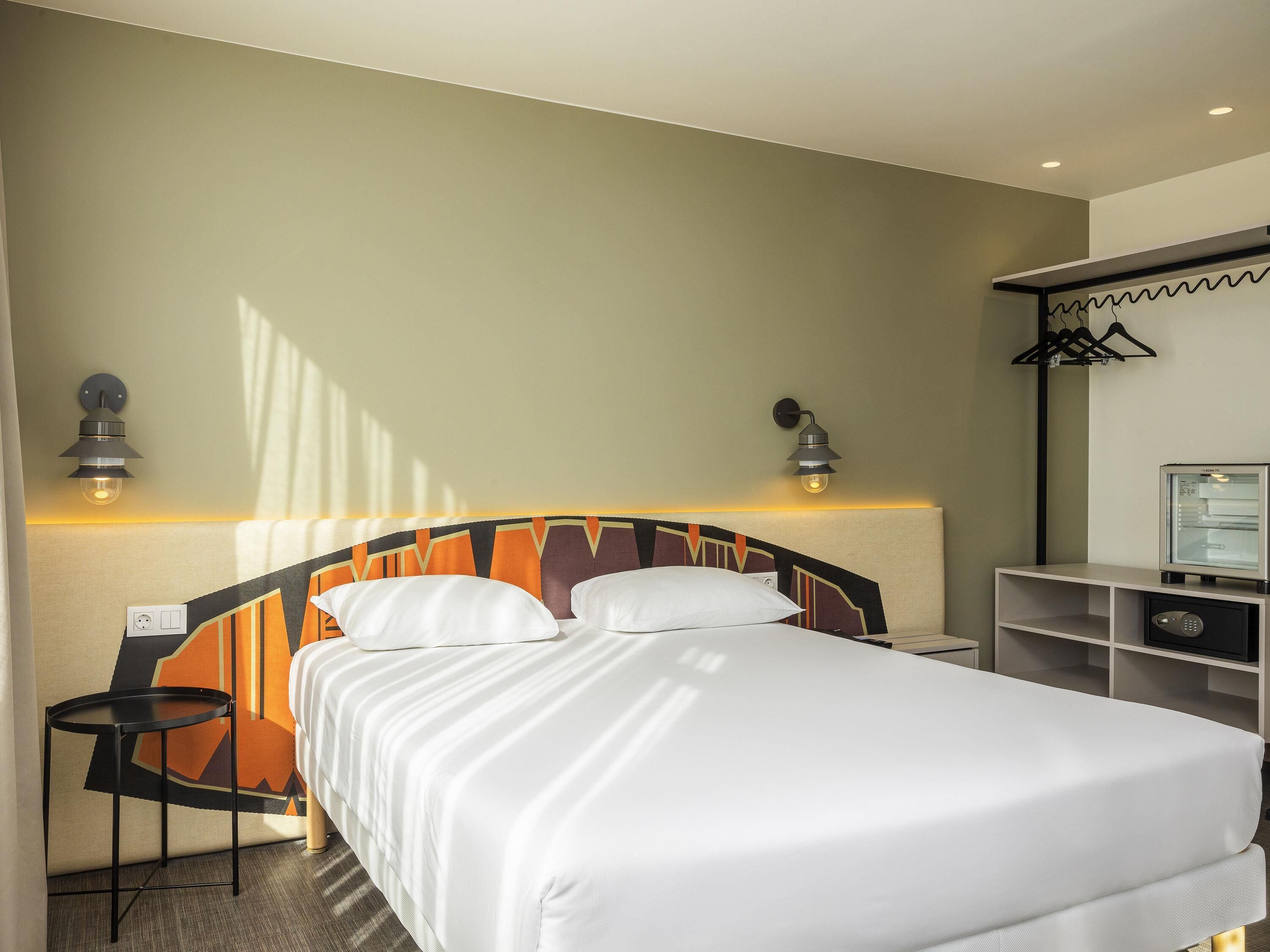 Una habitación de hotel con una cama, mesitas de noche y un escritorio con refrigerador.