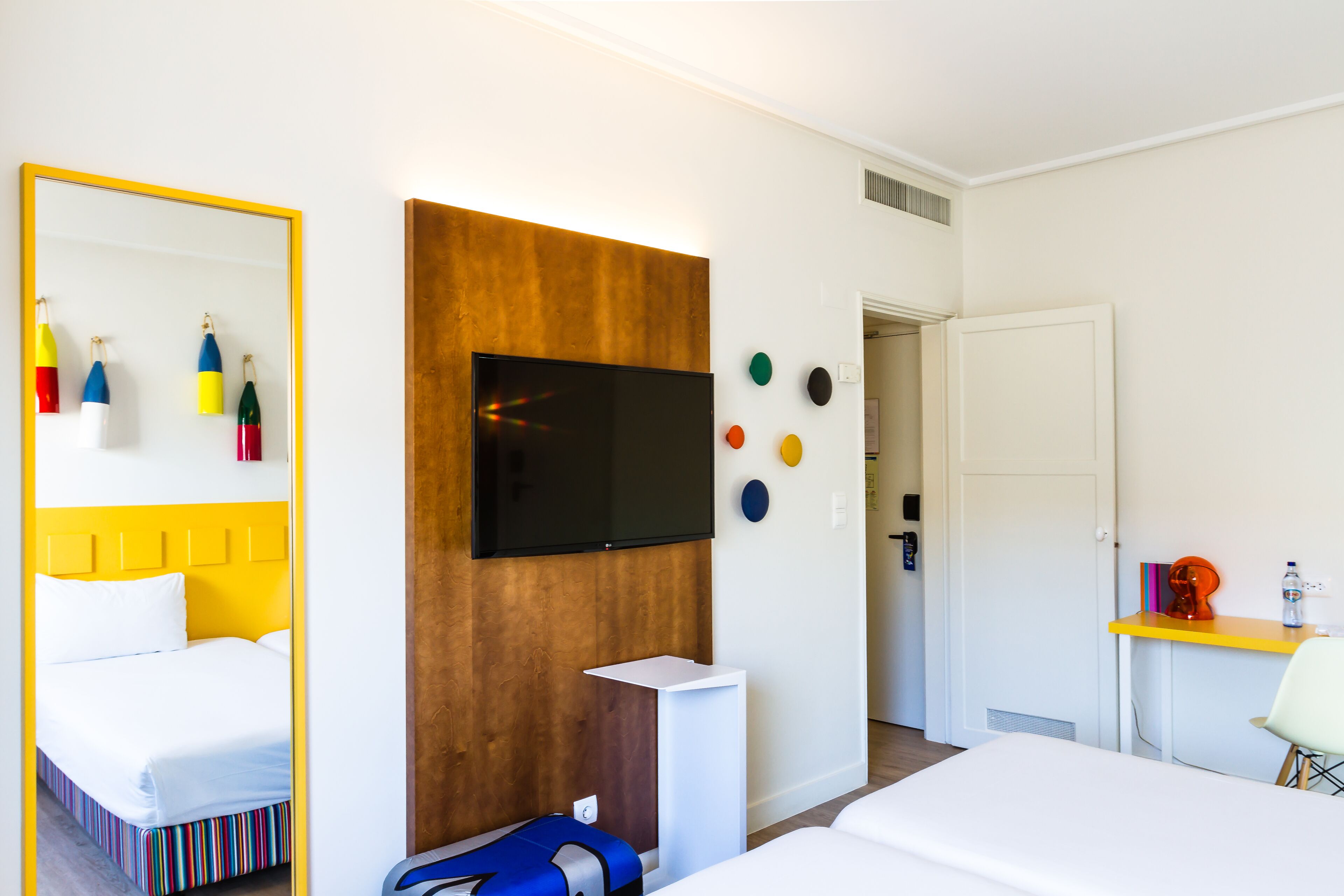 Une chambre d’hôtel comprenant un lit, un téléviseur fixé sur un panneau en bois, un bureau avec une chaise et une porte donnant sur une autre pièce.
