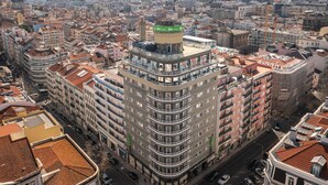 Un immeuble de grande hauteur doté de nombreux balcons, d’une enseigne verte bien visible et offrant une vue sur le paysage urbain environnant.
