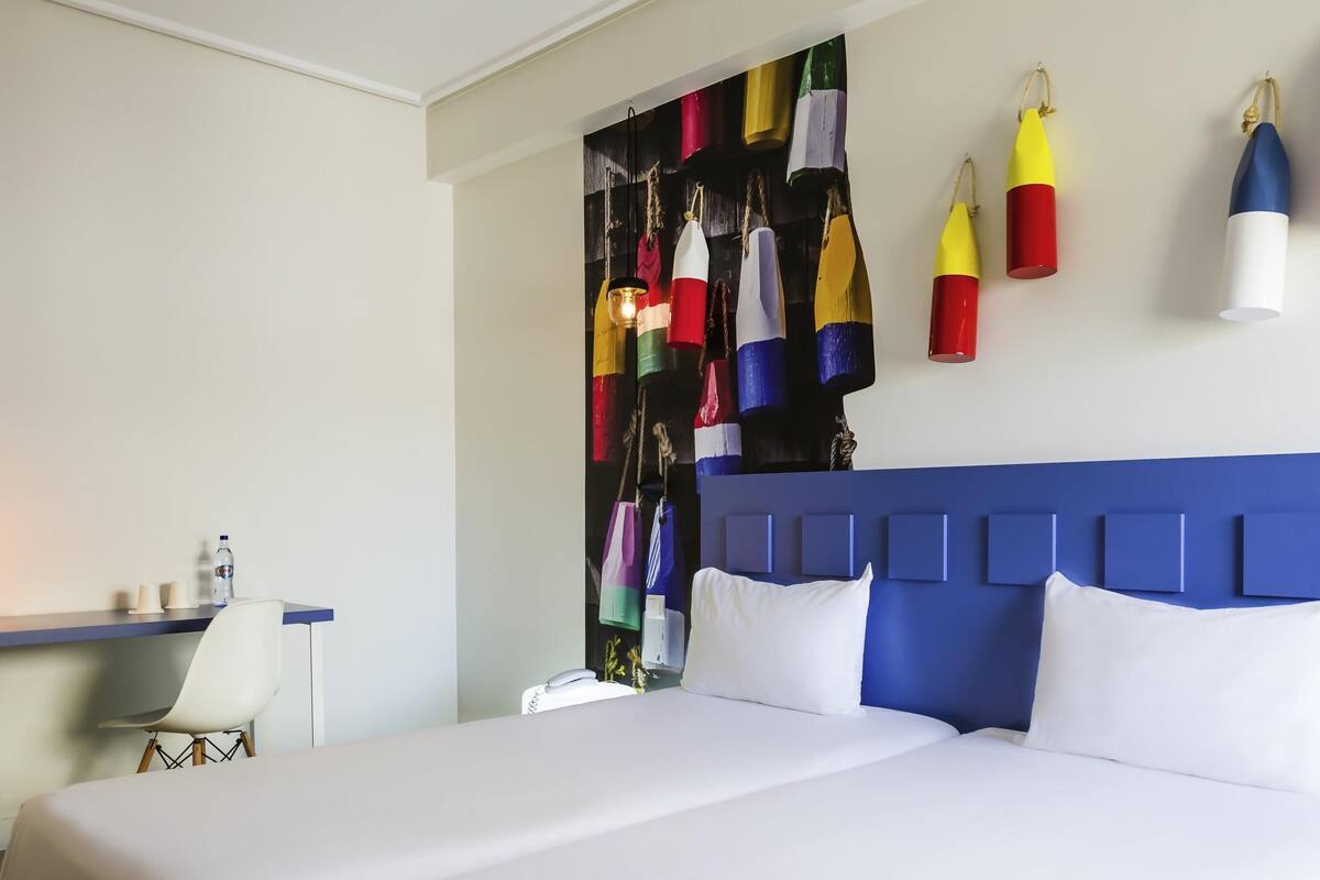Une chambre d’hôtel avec un grand lit, un bureau avec une chaise et un mur décoré d’objets colorés.