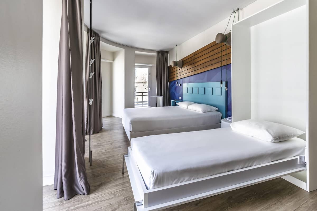 Une chambre d’hôtel moderne avec deux lits, un revêtement mural en bois au niveau de la tête de lit et une vue sur la ville.