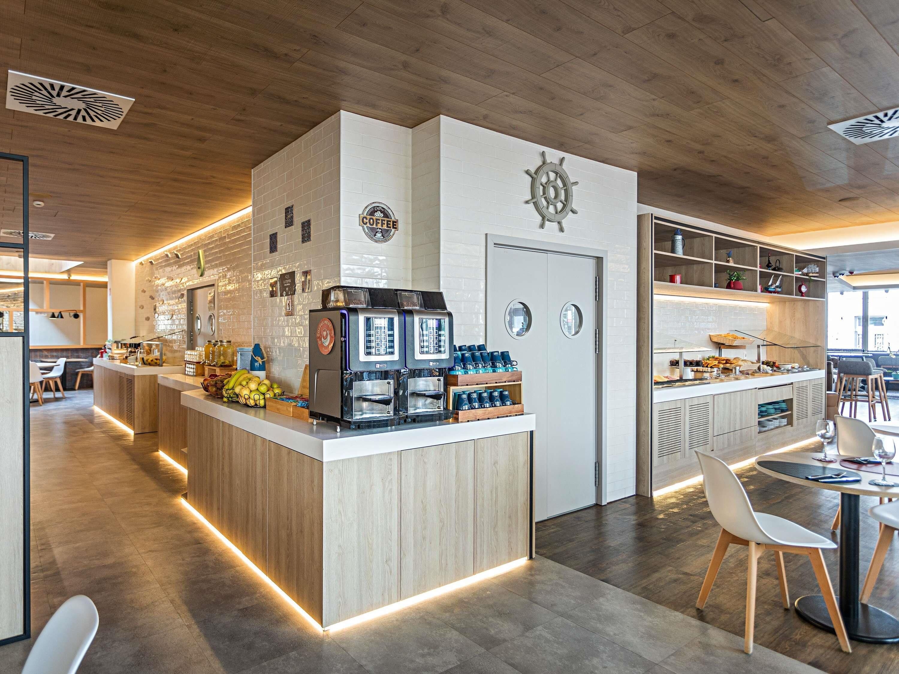 Un interno di caffetteria moderna con un bancone centrale, macchine per espresso e area salotto.