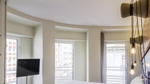 Une chambre d’hôtel moderne dotée d’un grand lit, d’un téléviseur à écran plat et offrant une vue sur la ville grâce à de grandes fenêtres.