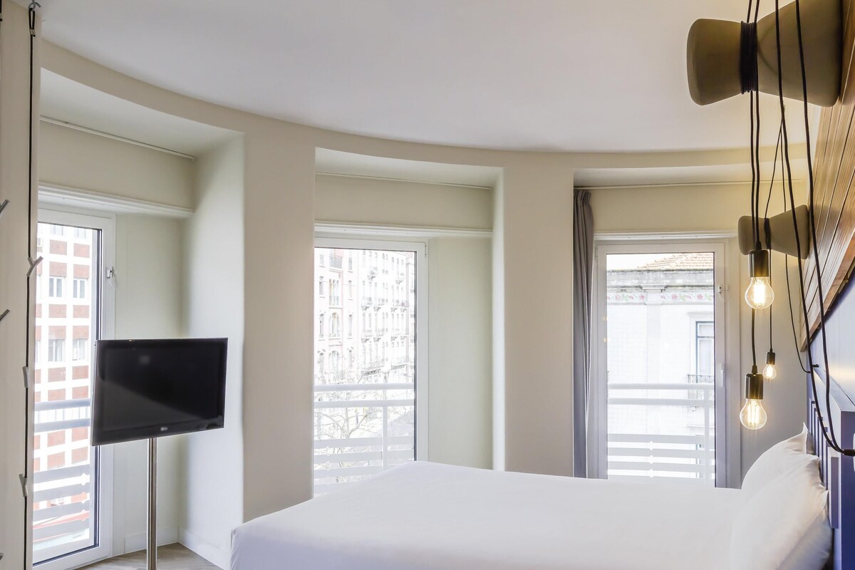 Een moderne hotelkamer met een groot bed, een flatscreen-tv en uitzicht op de stad door grote ramen.