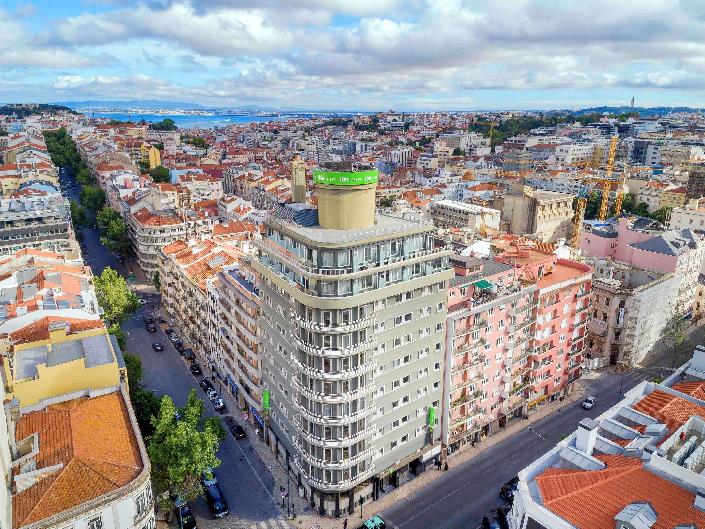 A multi-story building with a central courtyard, surrounded by other buildings, and a view of the cityscape in the background.