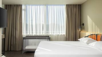 A hotel room with a bed, a desk, a chair, and a window with curtains.