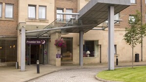 Entrada de hotel con una cubierta de vidrio, un letrero de Premier Inn y una cesta de flores.