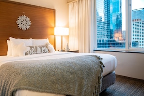 A hotel room with a large bed, a nightstand with a lamp, a decorative snowflake, and a view of a cityscape through the window. - Embassy Suites by Hilton Chicago Downtown Magnificent Mile (Chicago)