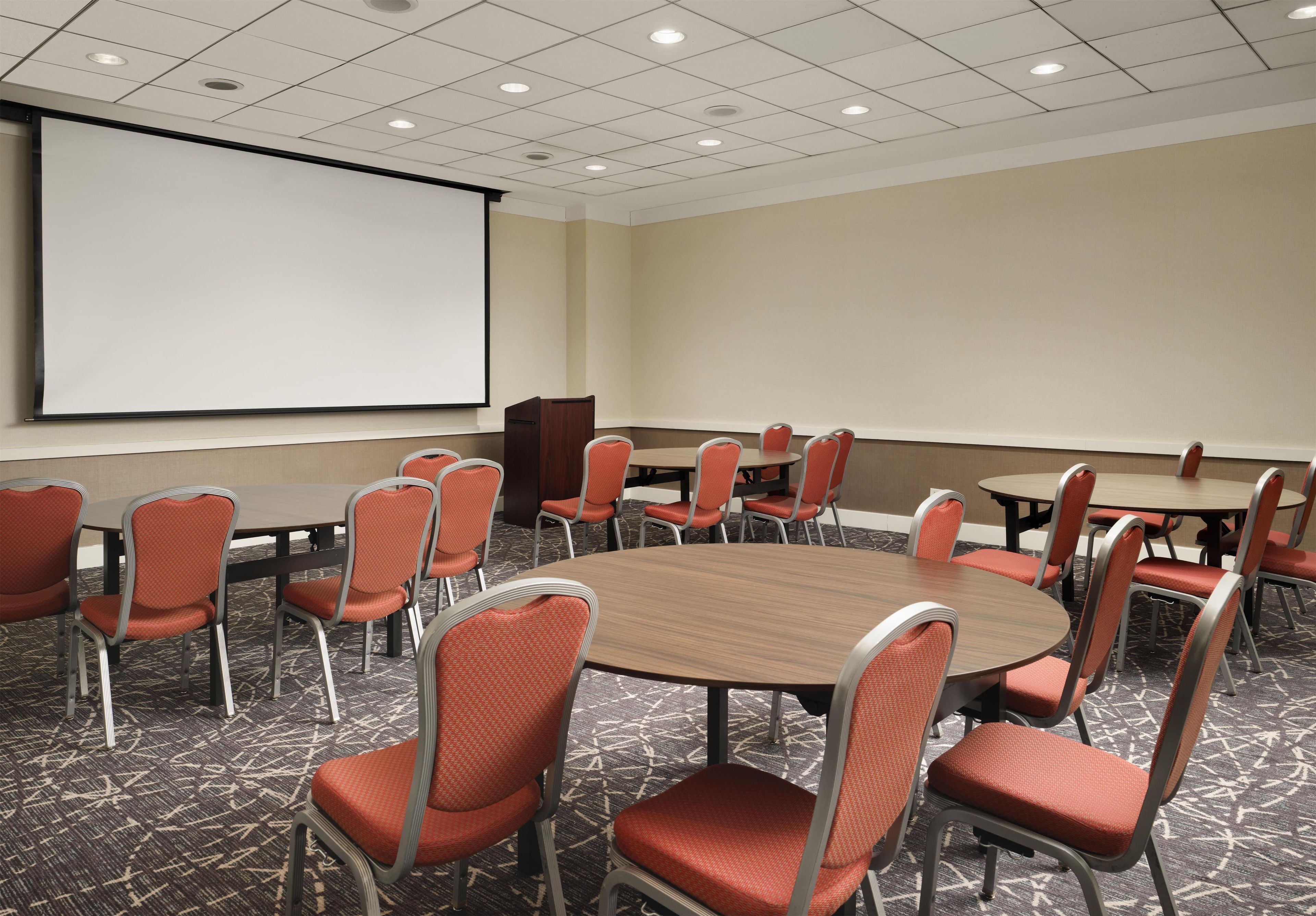 A conference room with a large screen, multiple tables, and chairs.